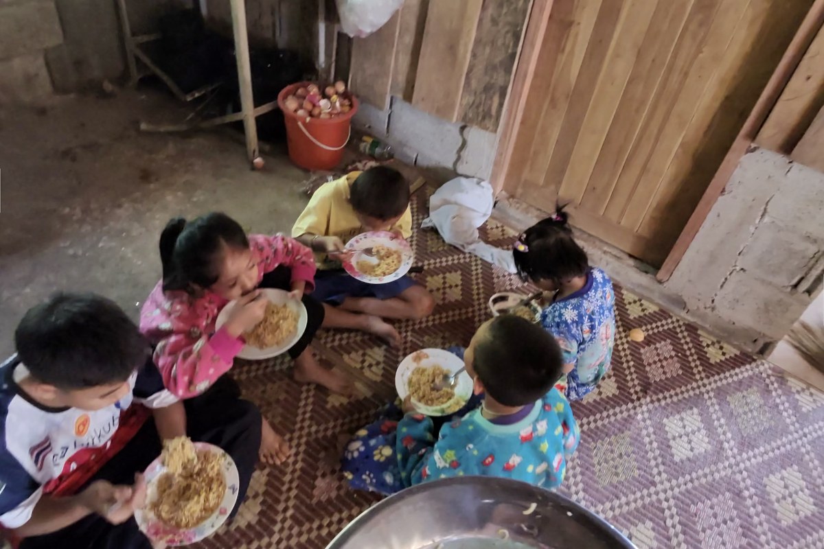 Village children sharing a noodle meal together on a woven mat