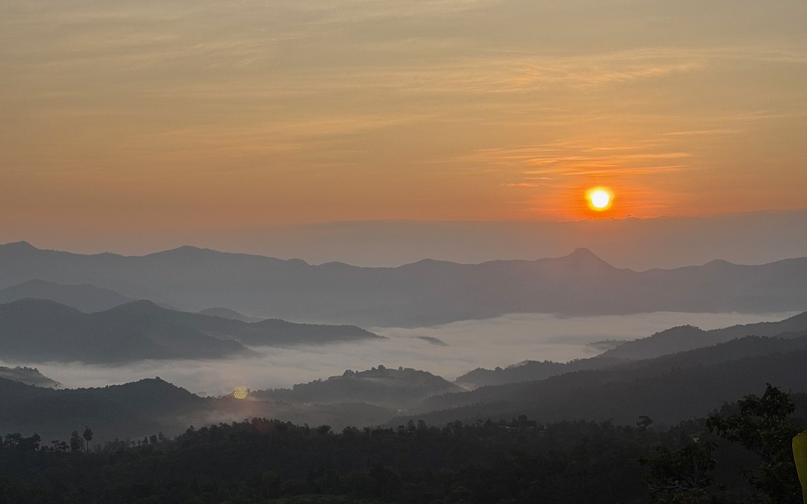 Sun setting over layered mountains and mist in the valley