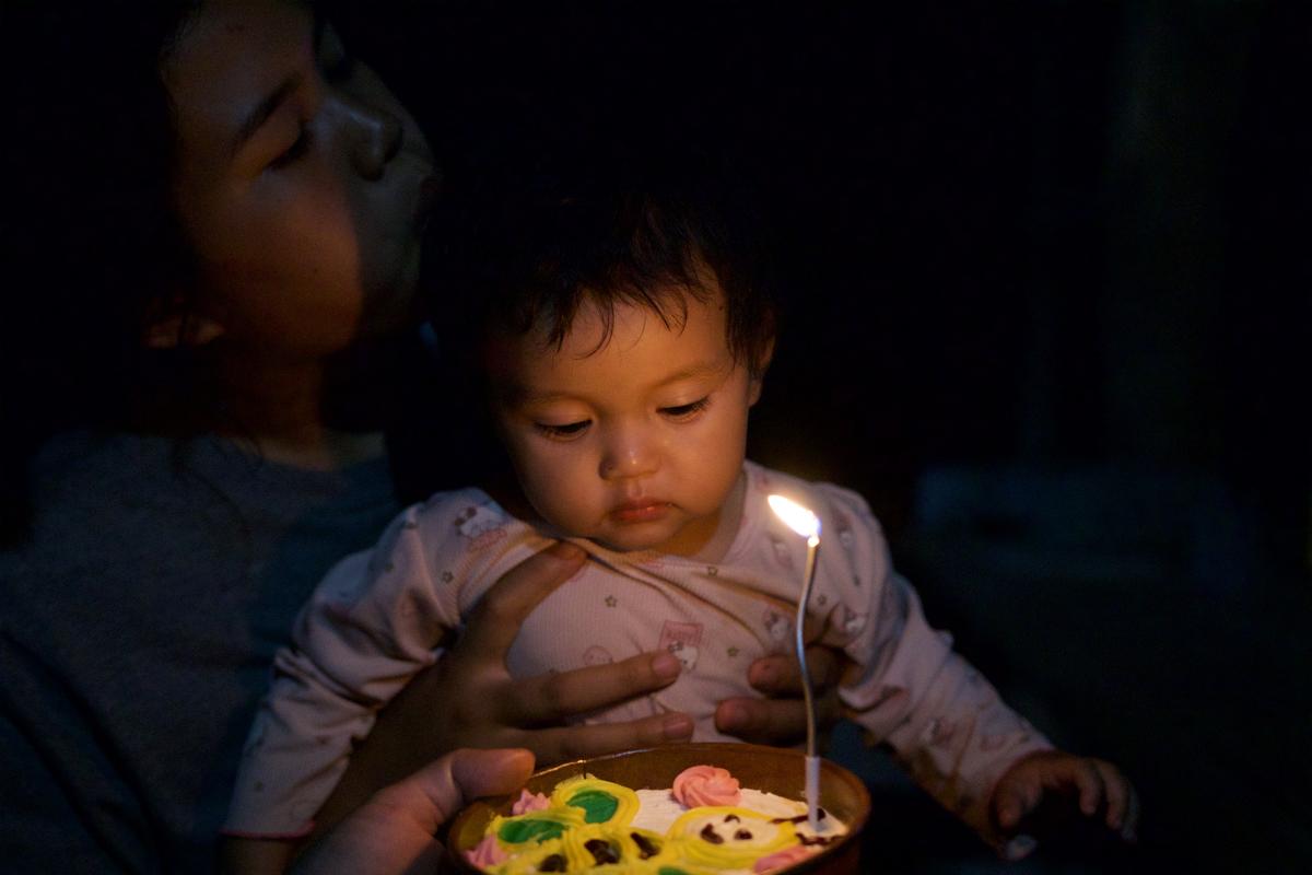 A baby looking at a candlelit birthday cake